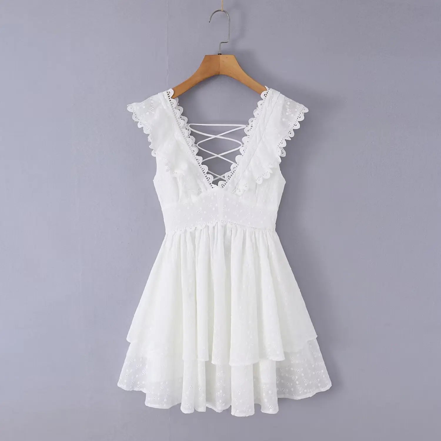 Front view of the white eyelet dress hanging on a wooden hanger, showing the full silhouette and ruffled neckline