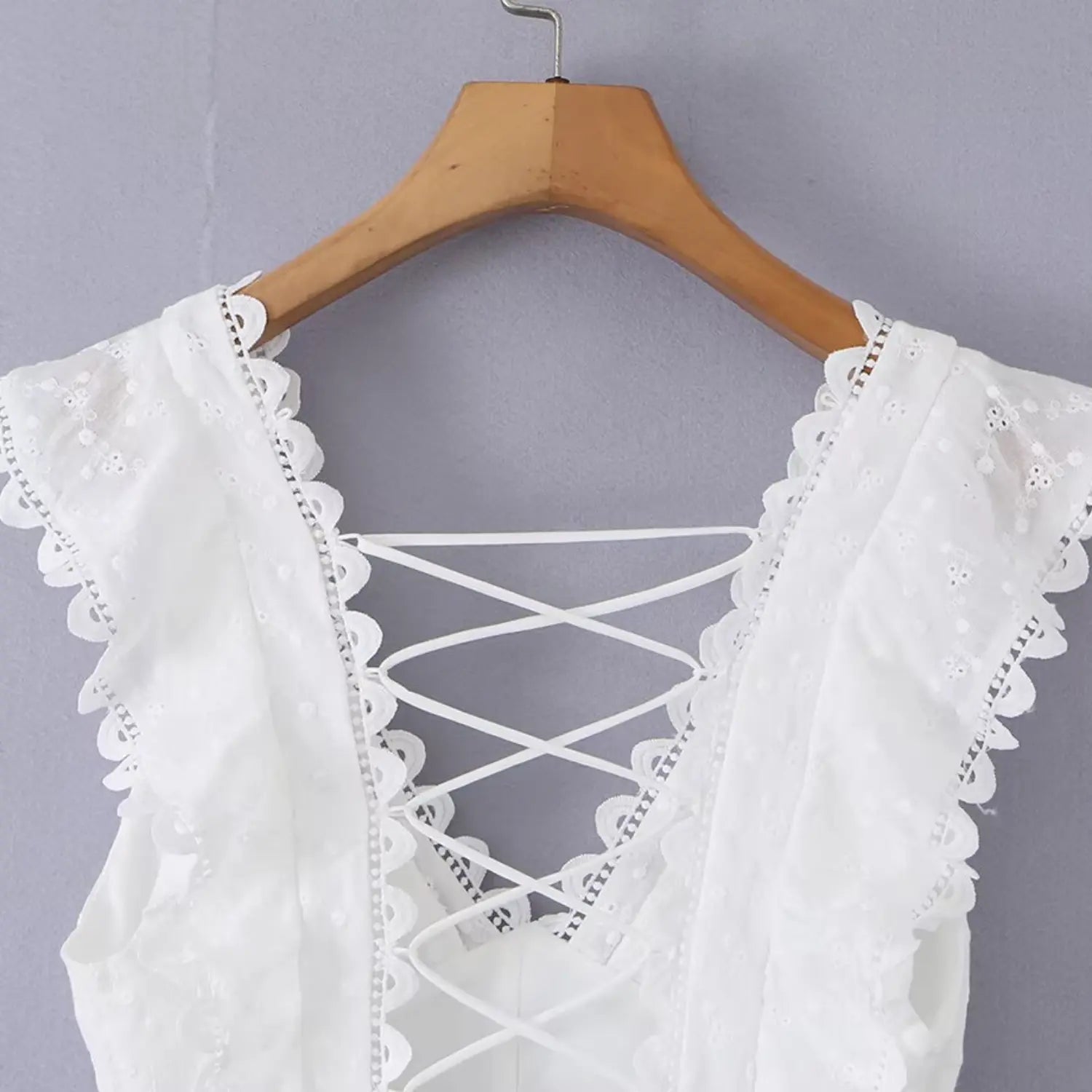Close-up shot of the deep V-neckline with ruffled lace trim and crisscross back tie detail on a white eyelet dress