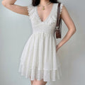 Lifestyle shot of a woman wearing the white eyelet lace dress, paired with a brown handbag