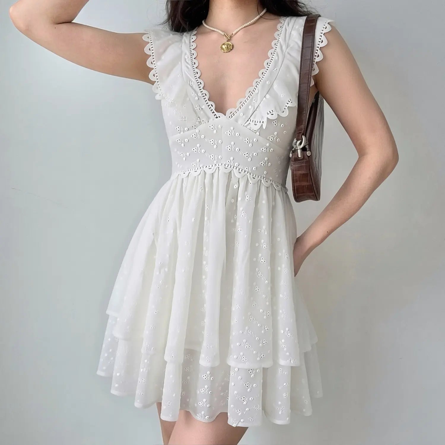 Lifestyle shot of a woman wearing the white eyelet lace dress, paired with a brown handbag