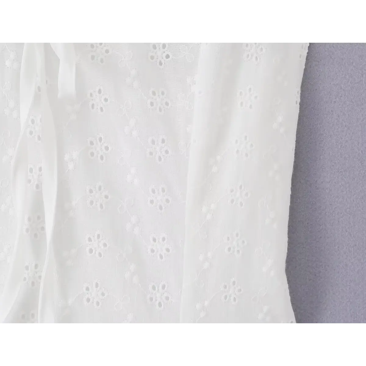 Close-up of the eyelet embroidery and lightweight fabric texture on the white dress bodice