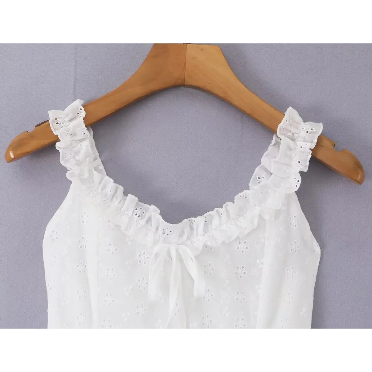 Close-up of the ruffled neckline, bow detail, and eyelet embroidery on the white cami dress