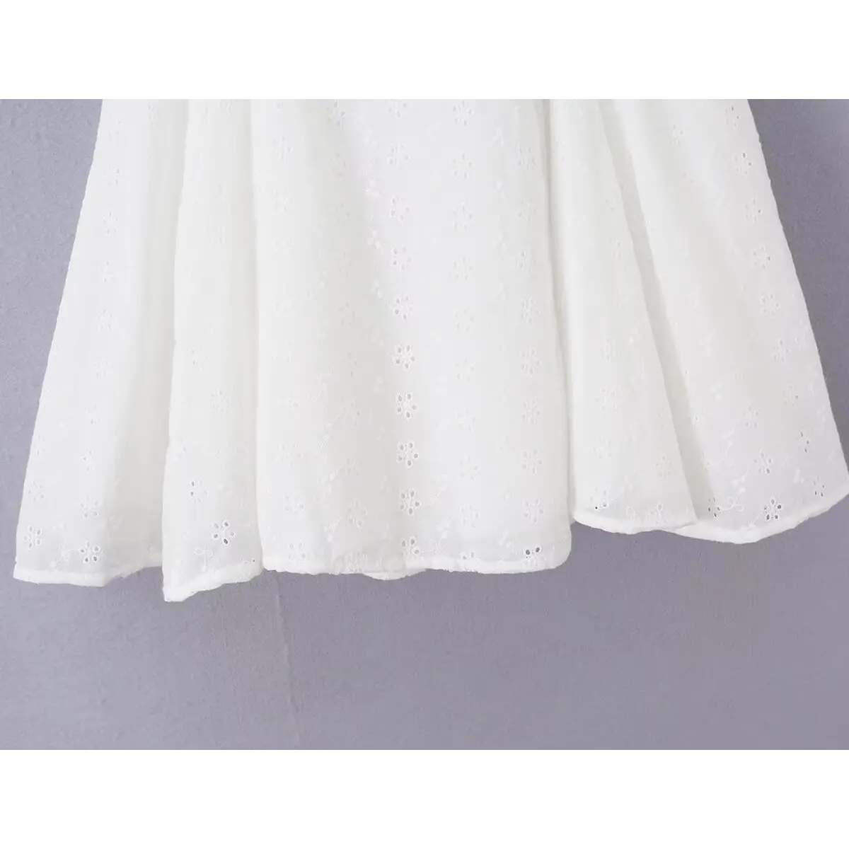Close-up of the flared skirt hem and eyelet fabric texture on the white dress