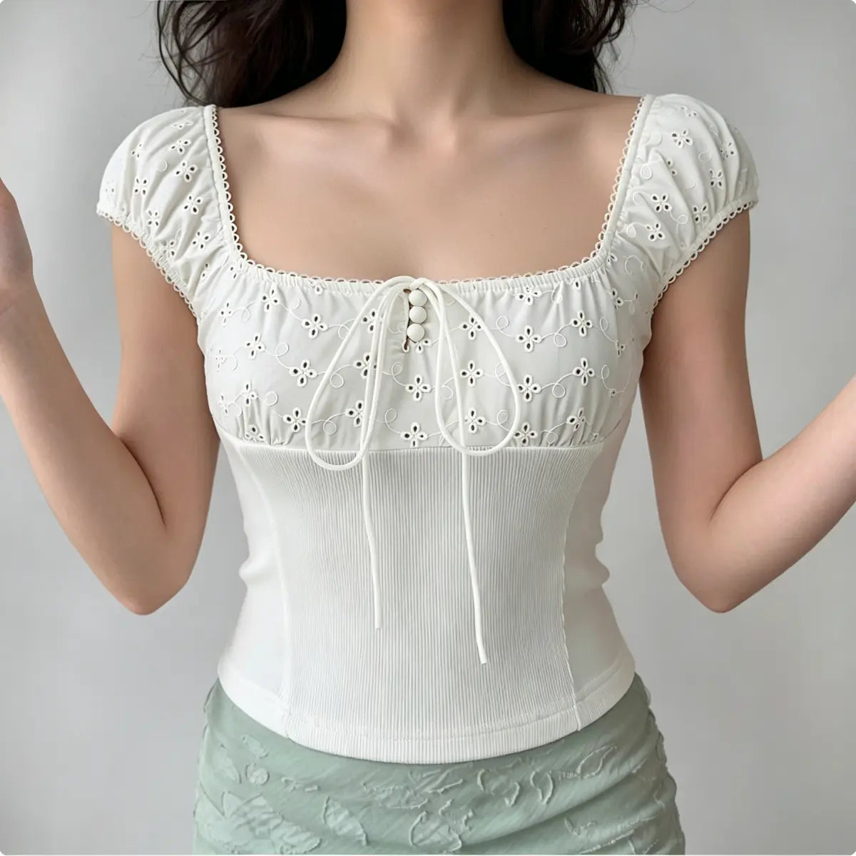 Model wearing white eyelet embroidered bustier top with square neckline, drawstring tie, and ribbed corset-style body.