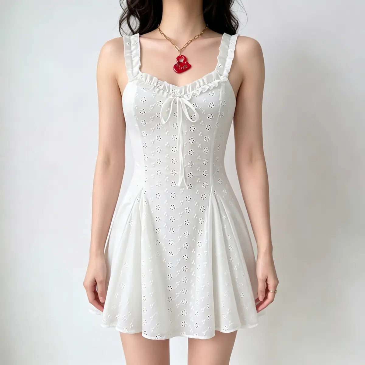 Model wearing a white eyelet-embroidered camisole mini dress with ruffled straps, a front bow detail, and a flared skirt.