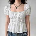 Model wearing a white eyelet-embroidered top with puffed sleeves, a square neckline, and a front tie detail, paired with jeans.