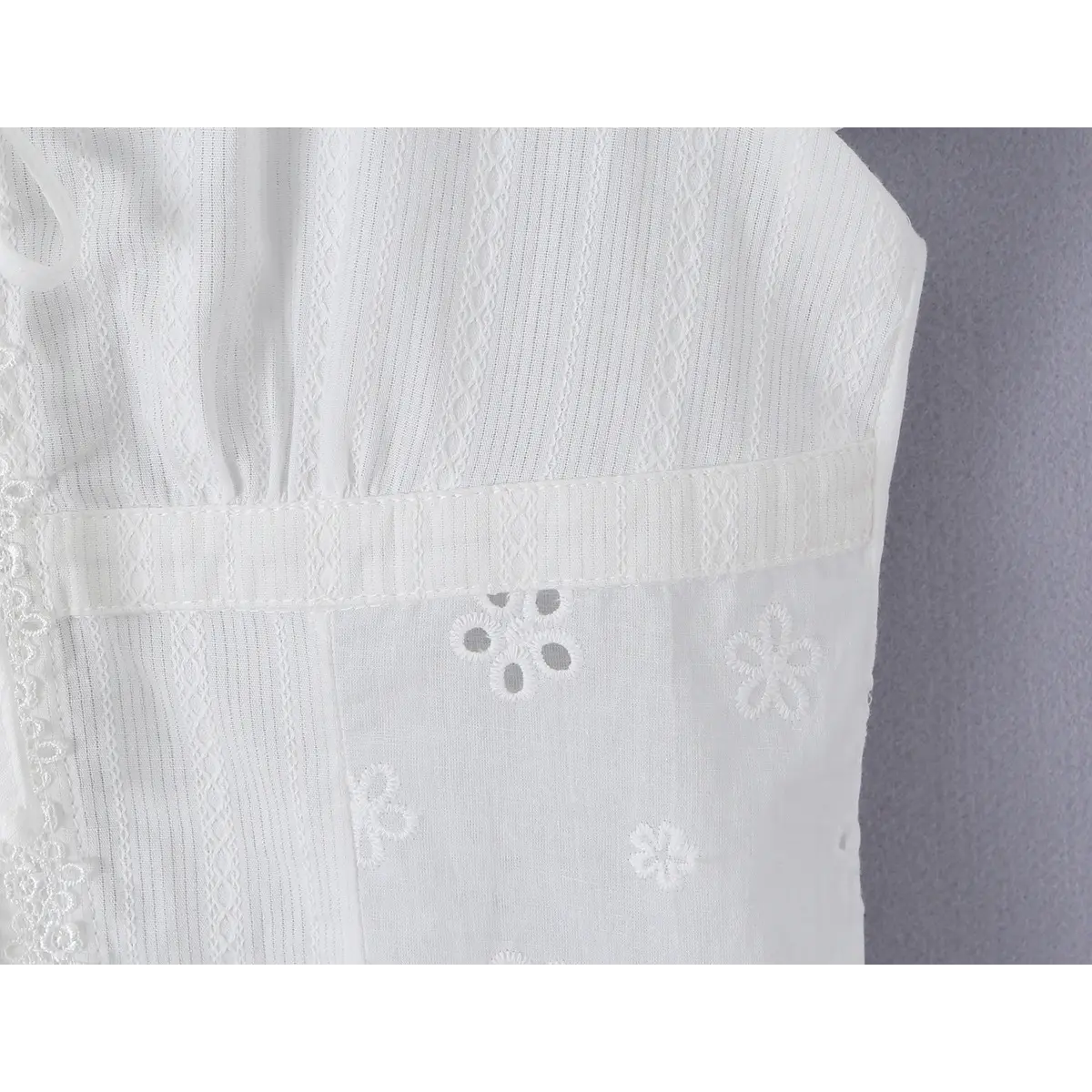 Close-up detail of the waist area on a white eyelet lace bustier shirt, showing the horizontal seam, vertical textured fabric, and floral eyelet embroidery.