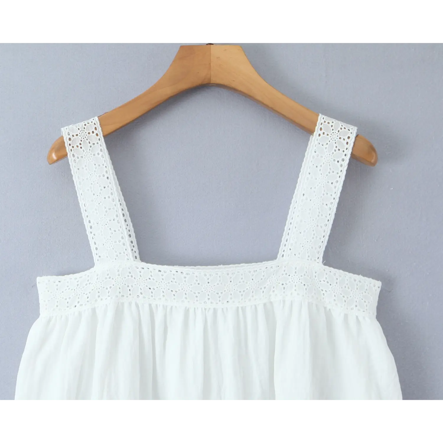 Close-up detail photo of eyelet lace shoulder straps and chest trim on white linen camisole top