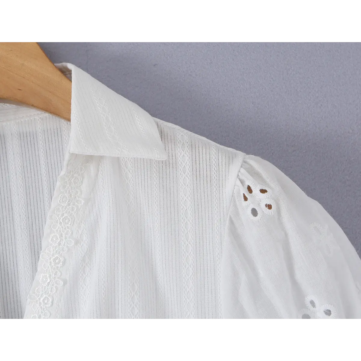 Close-up detail of the collar and shoulder of a white eyelet lace bustier shirt, showing the pointed collar, lace trim, and puff sleeve with eyelet embroidery.
