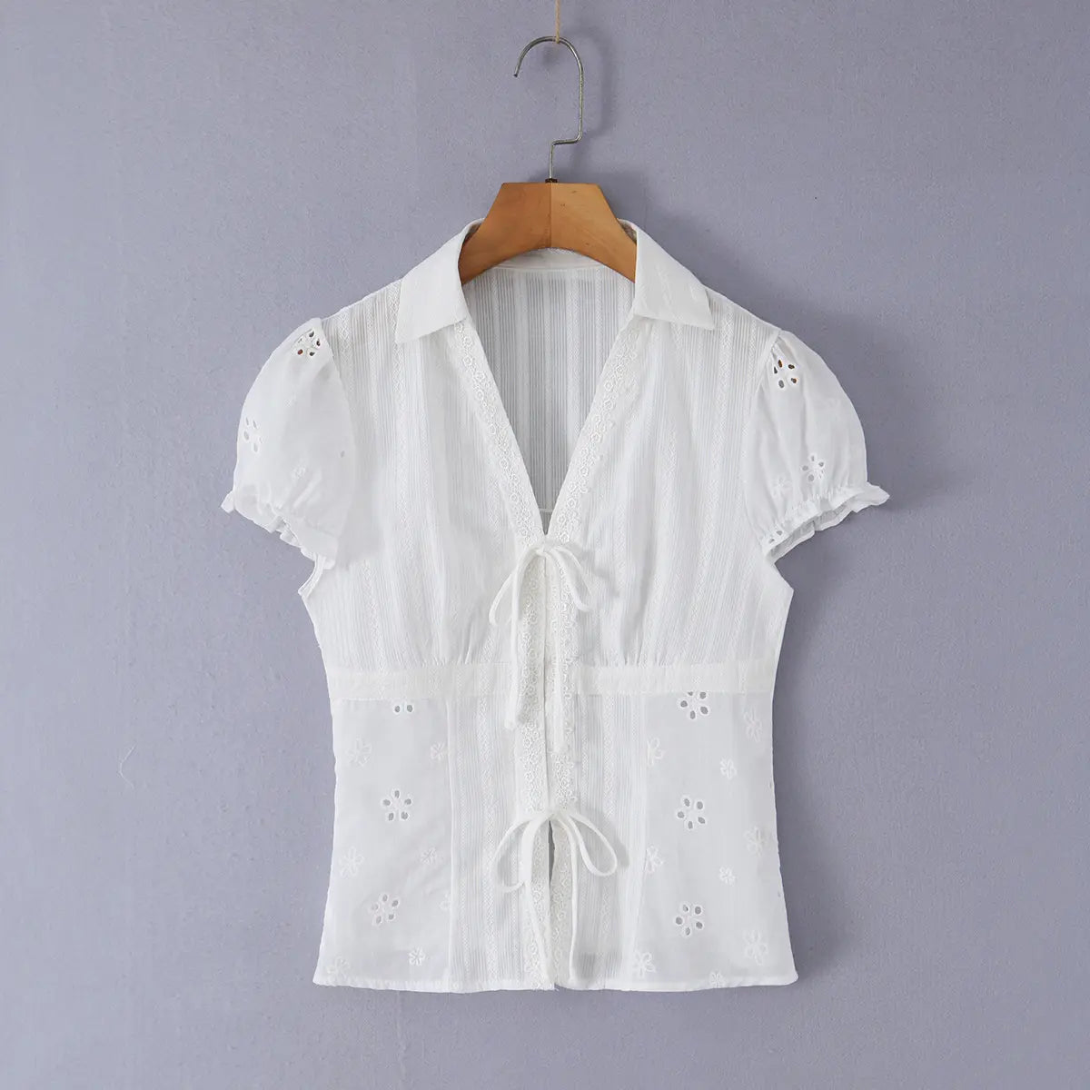 Front view of a white eyelet lace bustier shirt with puff sleeves, pointed collar, V-neck with lace trim, and two front tie closures.