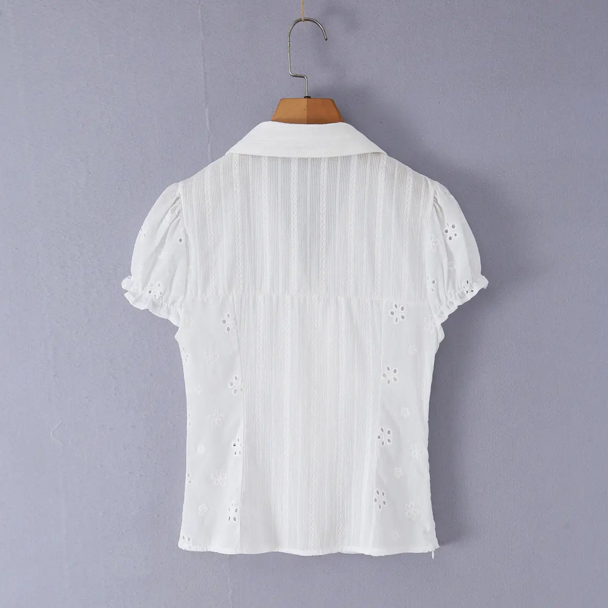 Back view of a white eyelet lace bustier shirt hung on a wooden hanger, showing the vertical textured fabric and puff sleeves.