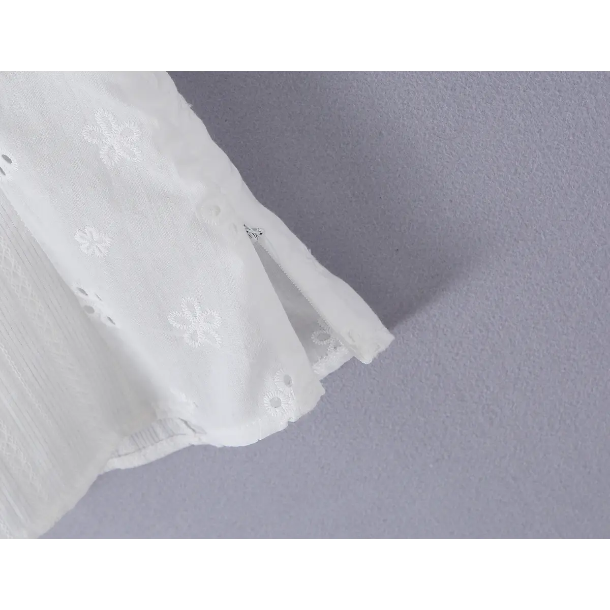 Close-up detail of the side zipper on a white eyelet lace bustier shirt, showing the eyelet embroidery and fabric construction.