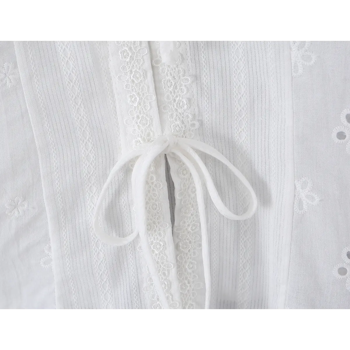 Close-up detail of the waist seam on a white eyelet lace bustier shirt, showing the eyelet embroidery, vertical textured fabric, and fitted construction.
