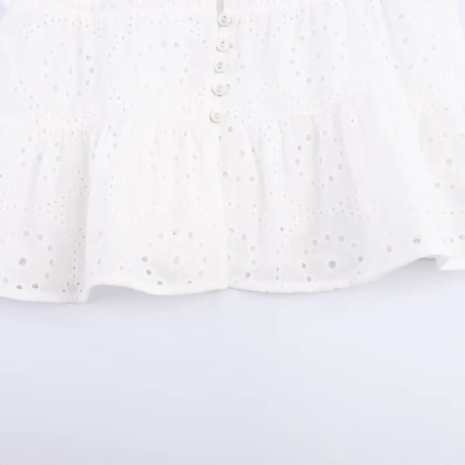 Close-up of the white shell buttons and tiered ruffle hem on the eyelet cami top