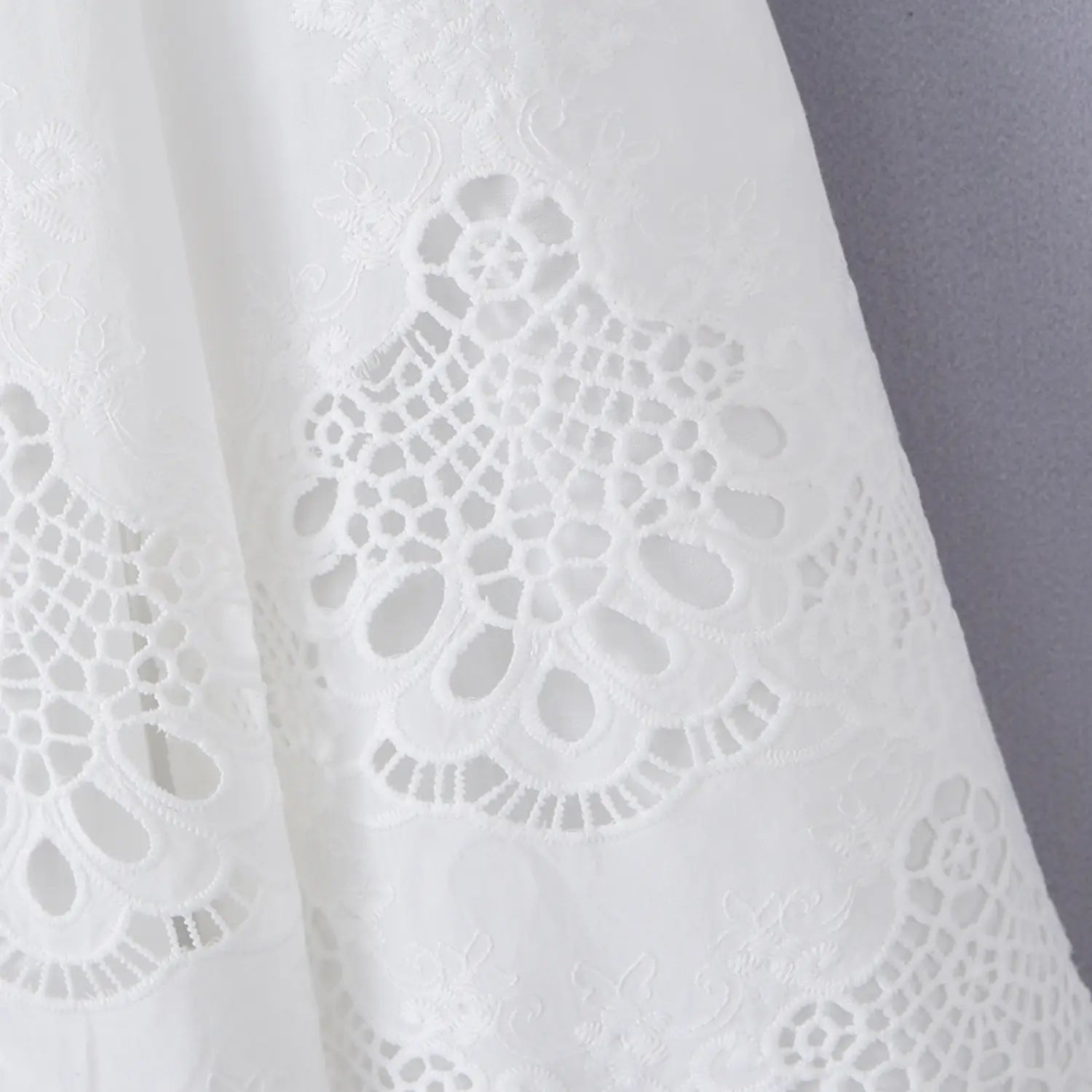 Close-up of the floral eyelet embroidery on the skirt hem of the white cotton dress