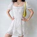 Lifestyle shot of model wearing the white square-neck puff-sleeve eyelet dress with floral embroidery, carrying a yellow handbag
