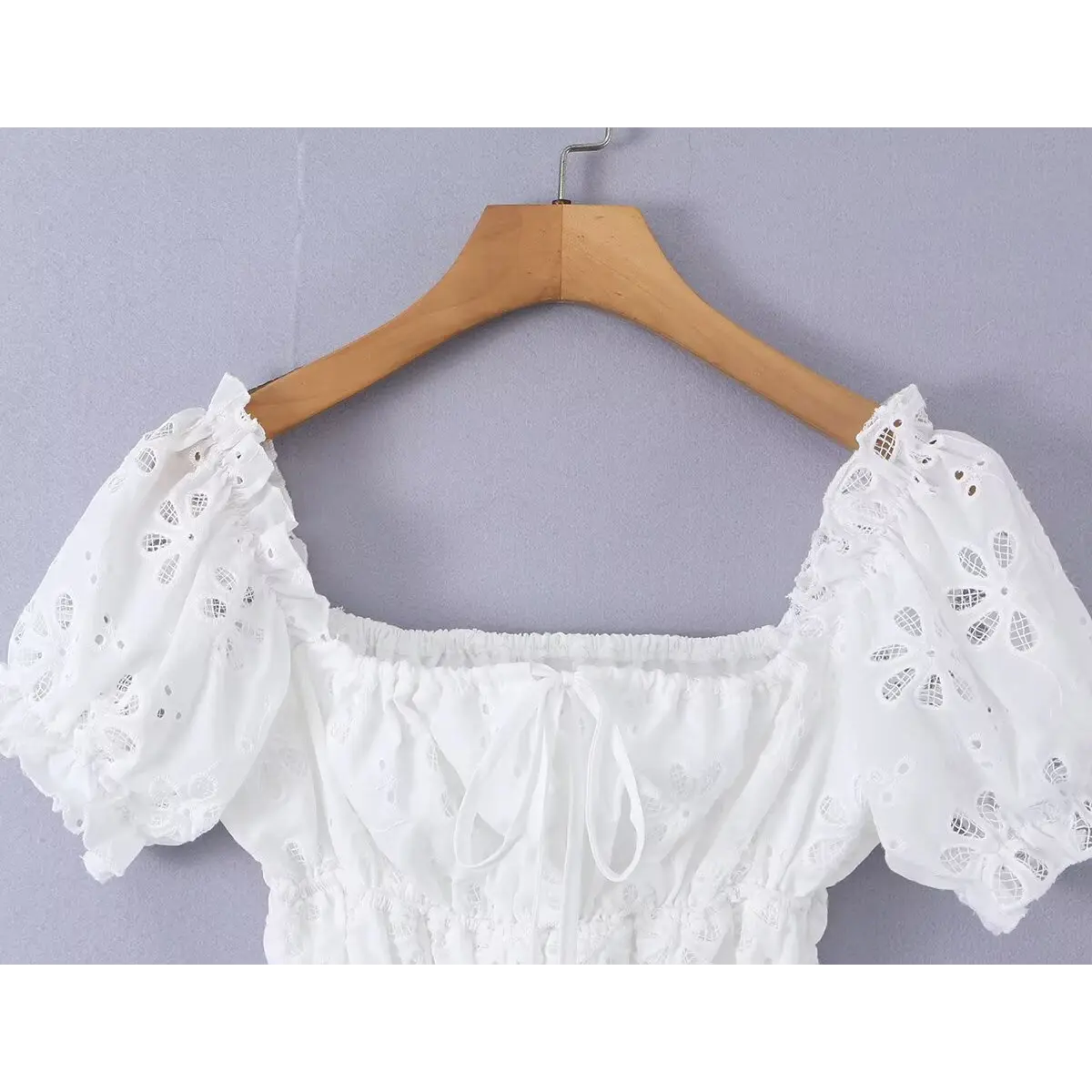 White eyelet embroidered top hanging on wooden hanger, showing the silhouette and puff sleeves