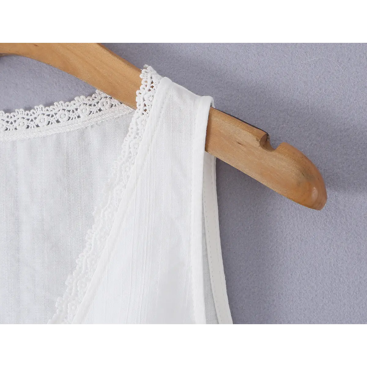  Close-up detail of the strap on a white ribbed bustier tank top, showing the lace-trimmed edge and wooden hanger.