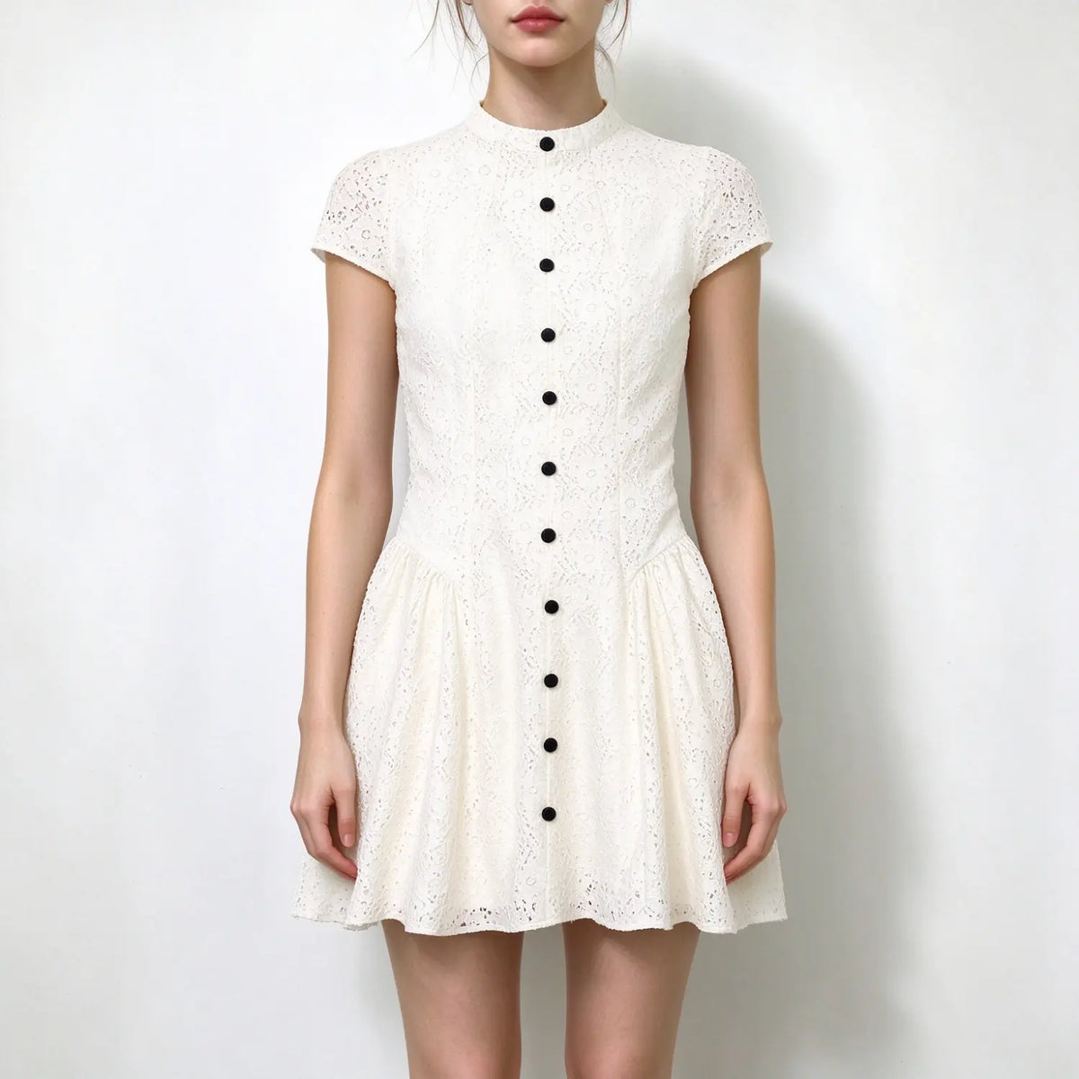 Model wearing white eyelet lace mini dress, stand collar, cap sleeves, front black button placket, fit and flare skirt, plain white background