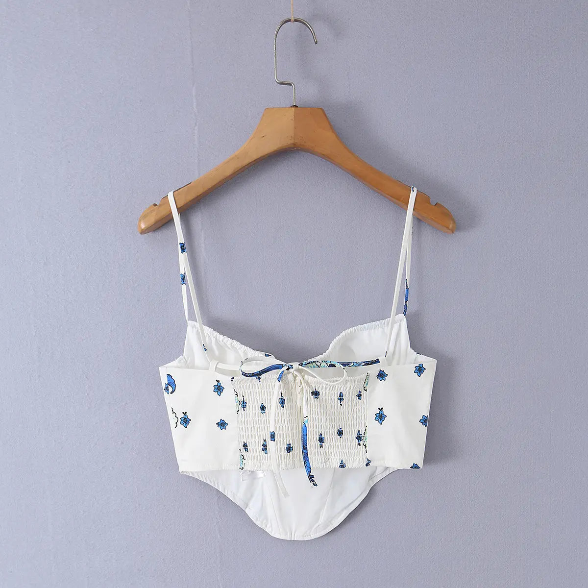 White cami top with blue floral print and tie closure, hanging on wooden hanger