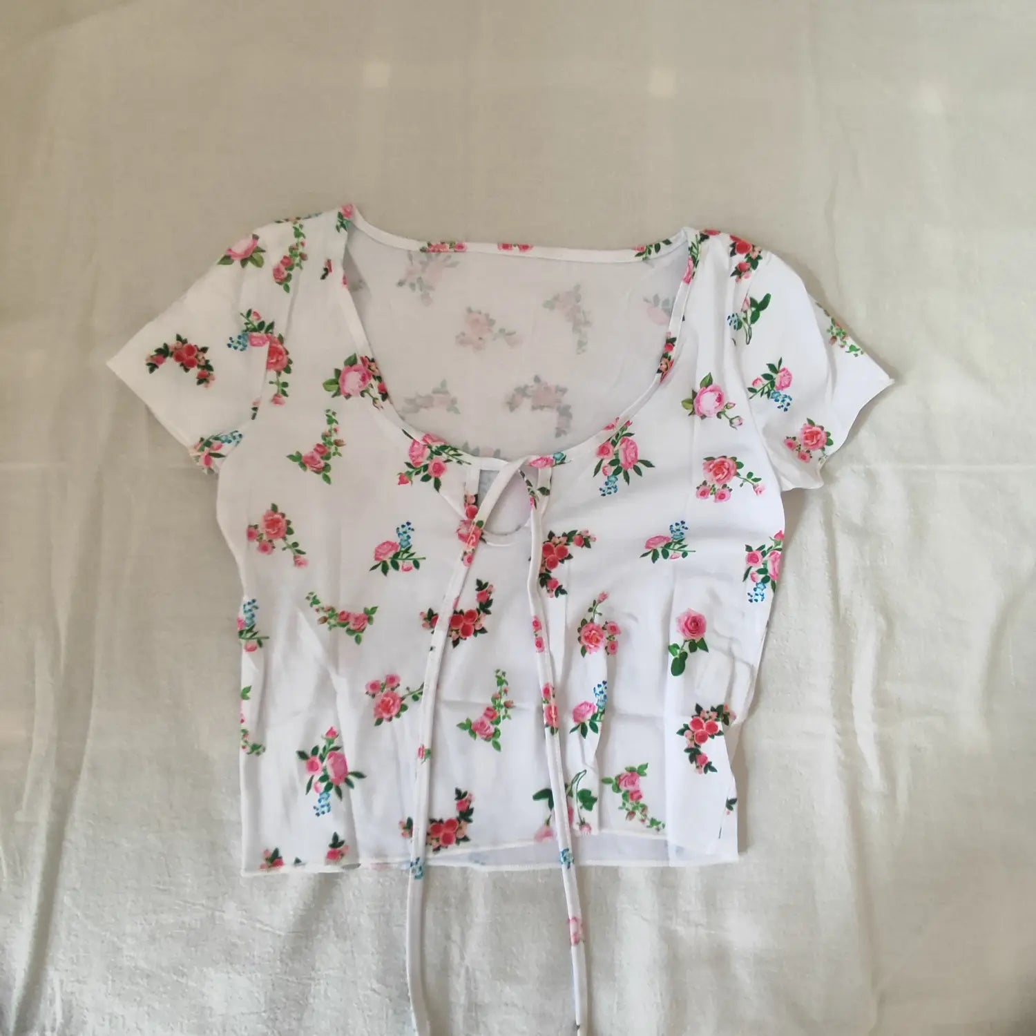 Flat lay full front view white short sleeve rose floral print tie‑keyhole cropped top