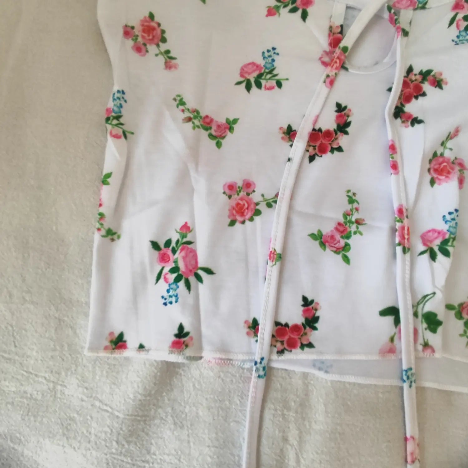 Flat lay close‑up bottom hem and front tie detail of white short sleeve floral rose print cropped top
