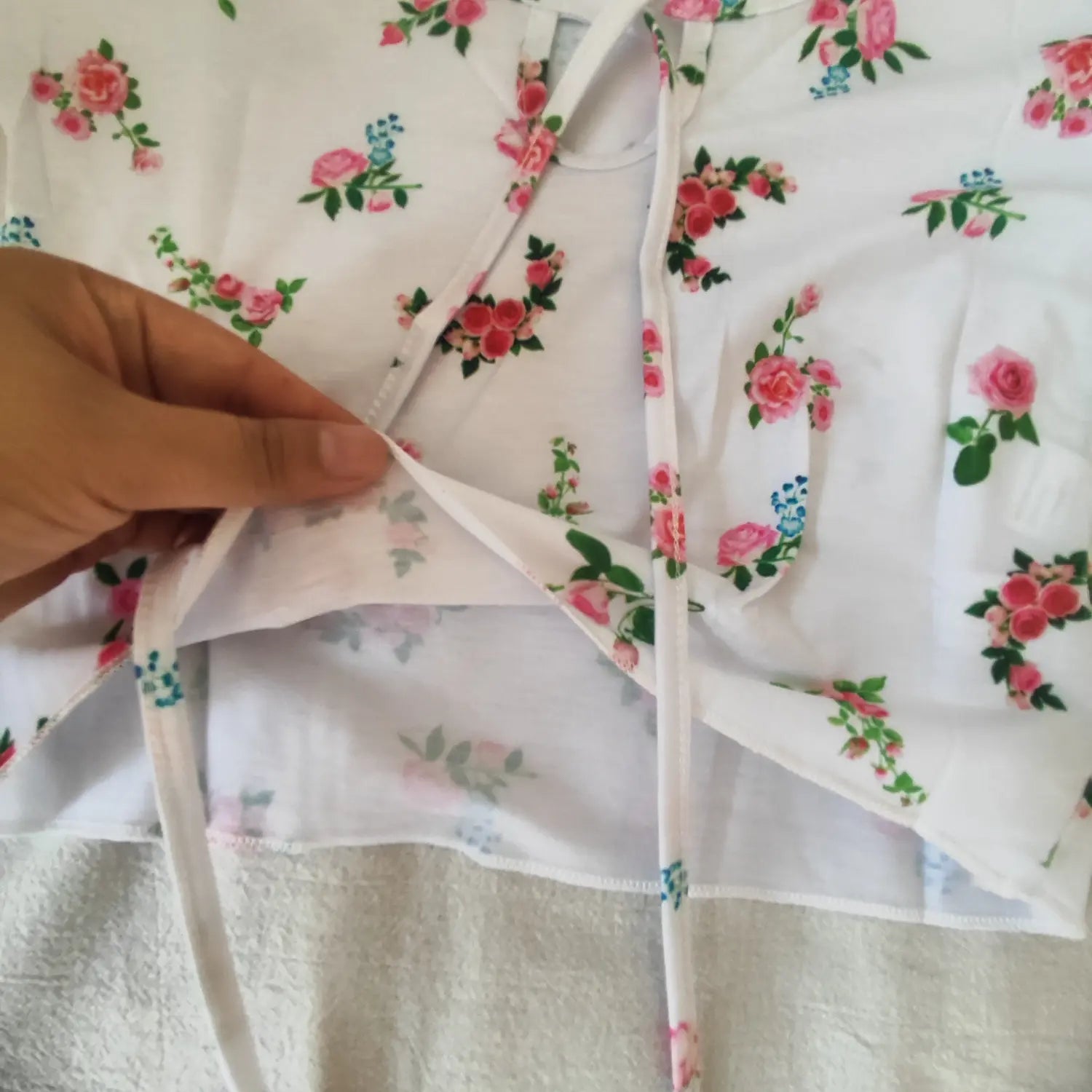 Hand lifting fabric to show front keyhole tie opening of white rose print cropped blouse