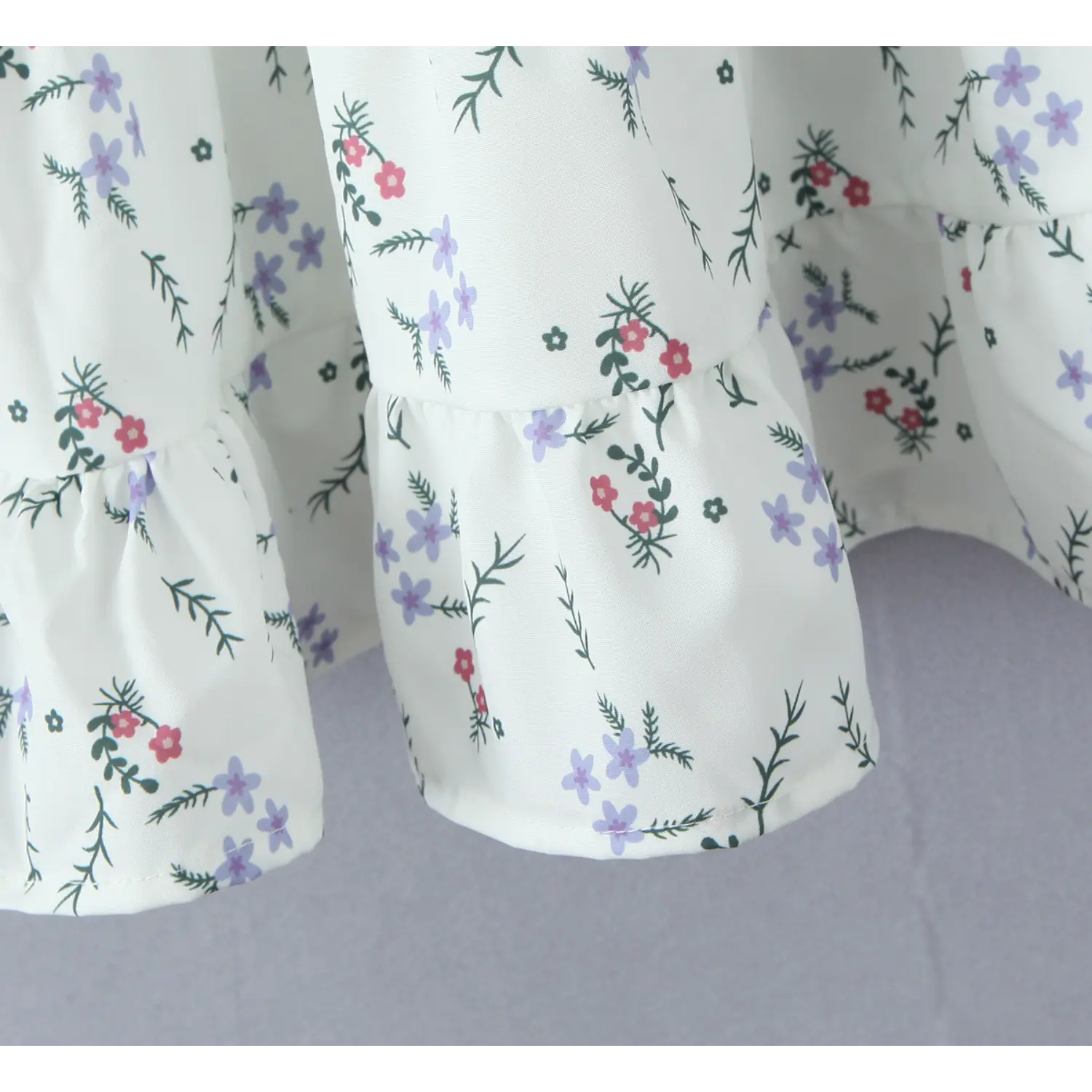 Macro shot of tiered ruffle skirt hem, finished seam, white fabric with purple and red ditsy floral pattern
