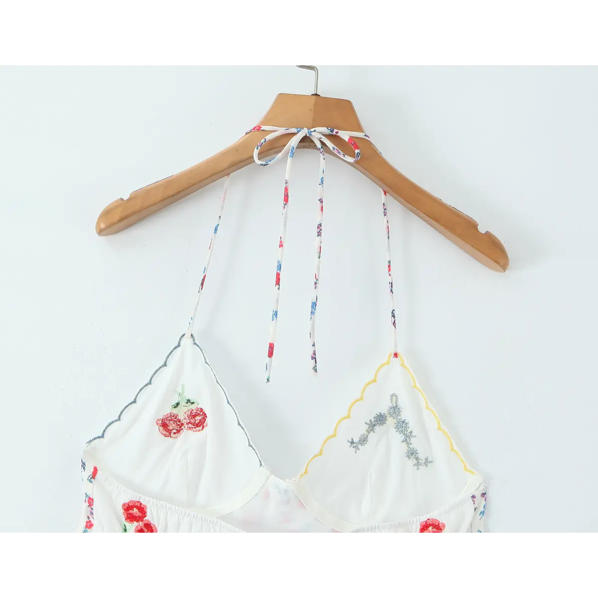 Partial view on wooden hanger of the floral slip dress showing the halter tie and embroidered cup details