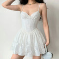 Lifestyle shot of model wearing white corset-style spaghetti strap mini dress with textured floral jacquard fabric, tucked-in fit and flared skirt
