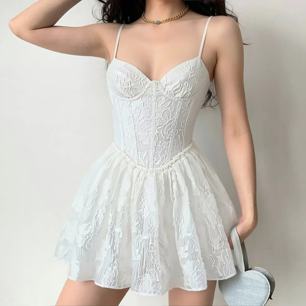 Lifestyle shot of model wearing white corset-style spaghetti strap mini dress with textured floral jacquard fabric, tucked-in fit and flared skirt
