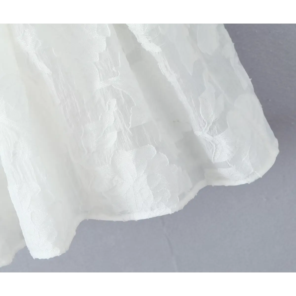 Close-up of the textured floral jacquard hem on the white dress skirt