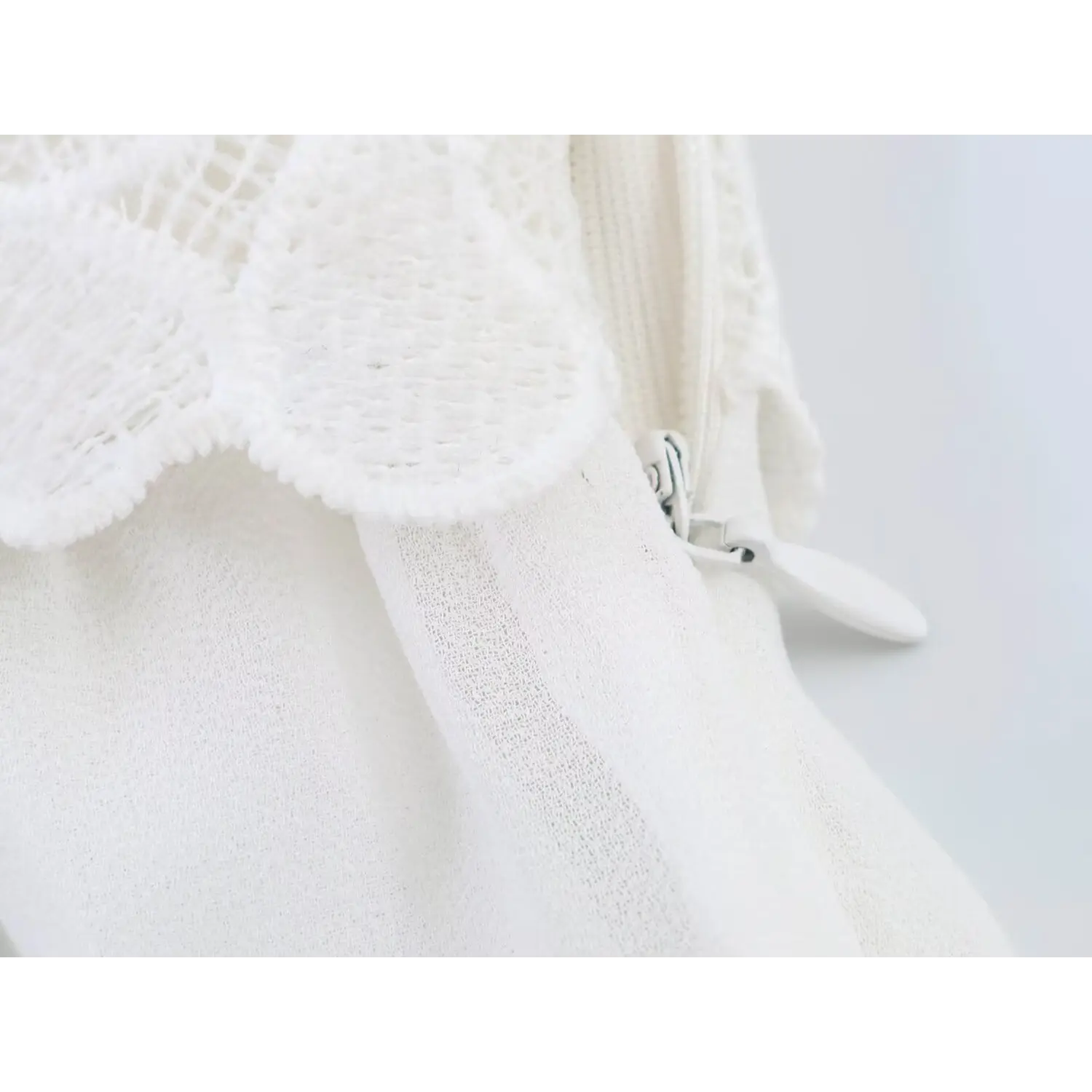 Macro shot of side invisible zipper with white fabric pull tab, layered hollow floral lace overlay above smooth chiffon