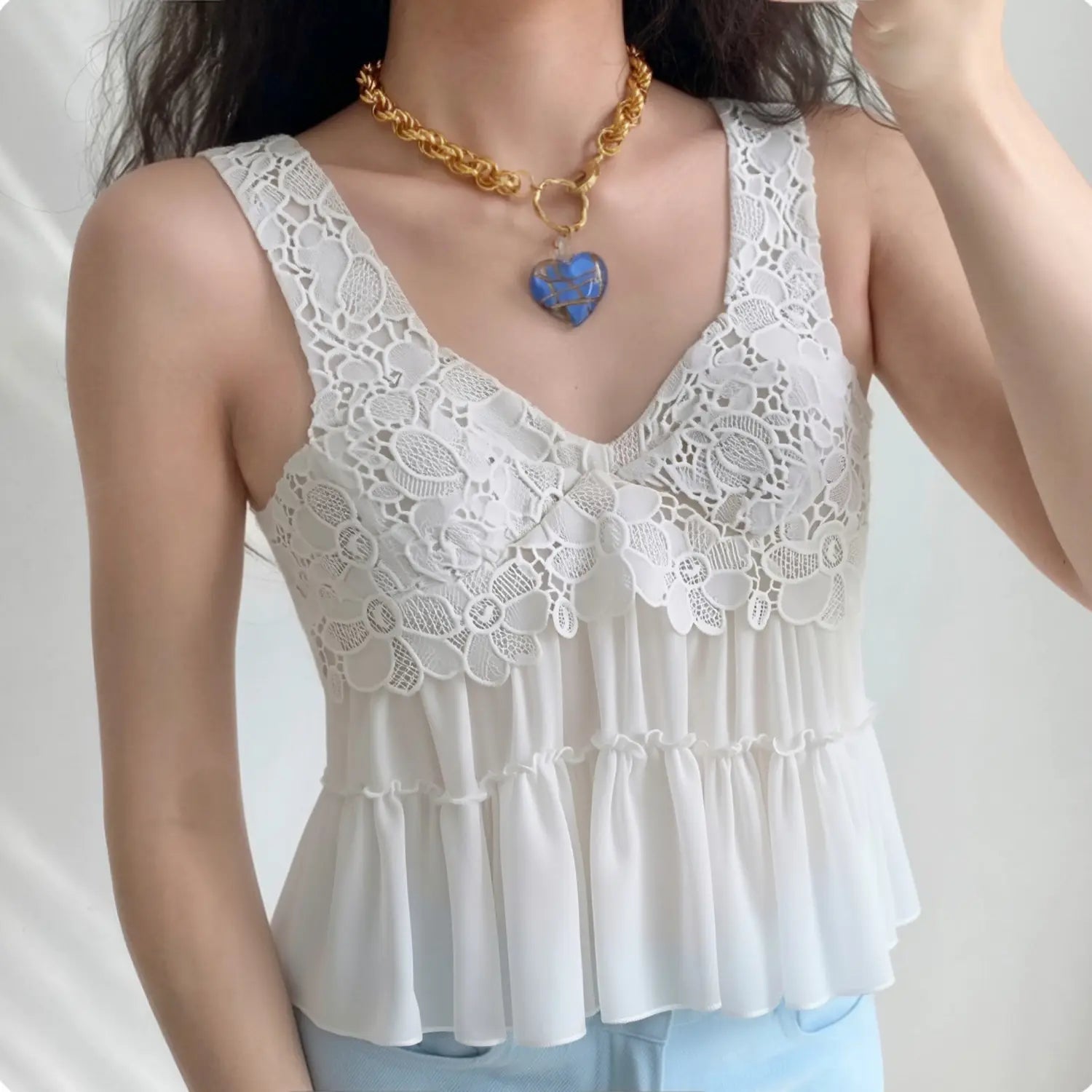 Lifestyle outfit photo of model wearing white lace peplum cami, paired with light blue denim jeans and oversized heart pendant gold chain necklace