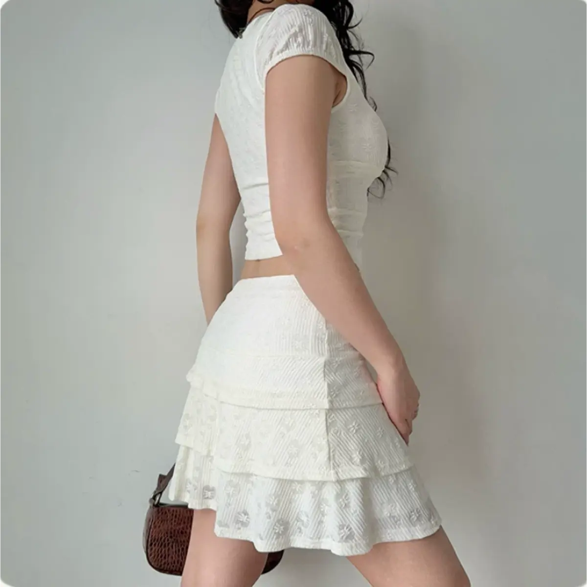 Close-up of the lace-up detail on a white floral lace cropped top, showing the textured fabric and square neckline.
