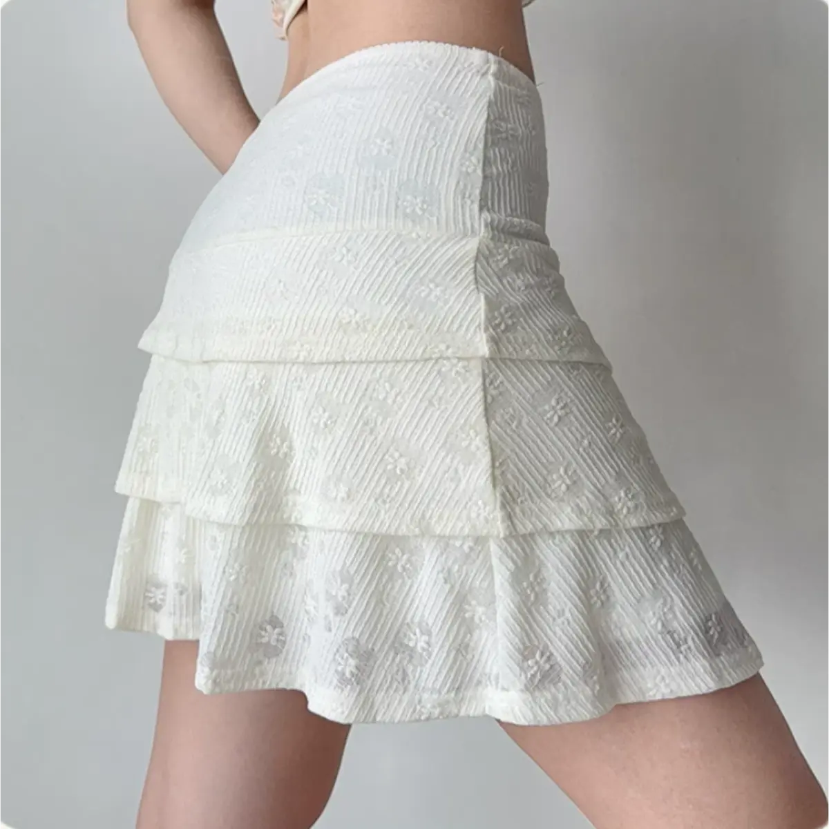 Back view of a woman in a white floral lace lace-up two-piece set, showing the cropped top and tiered skirt silhouette.
