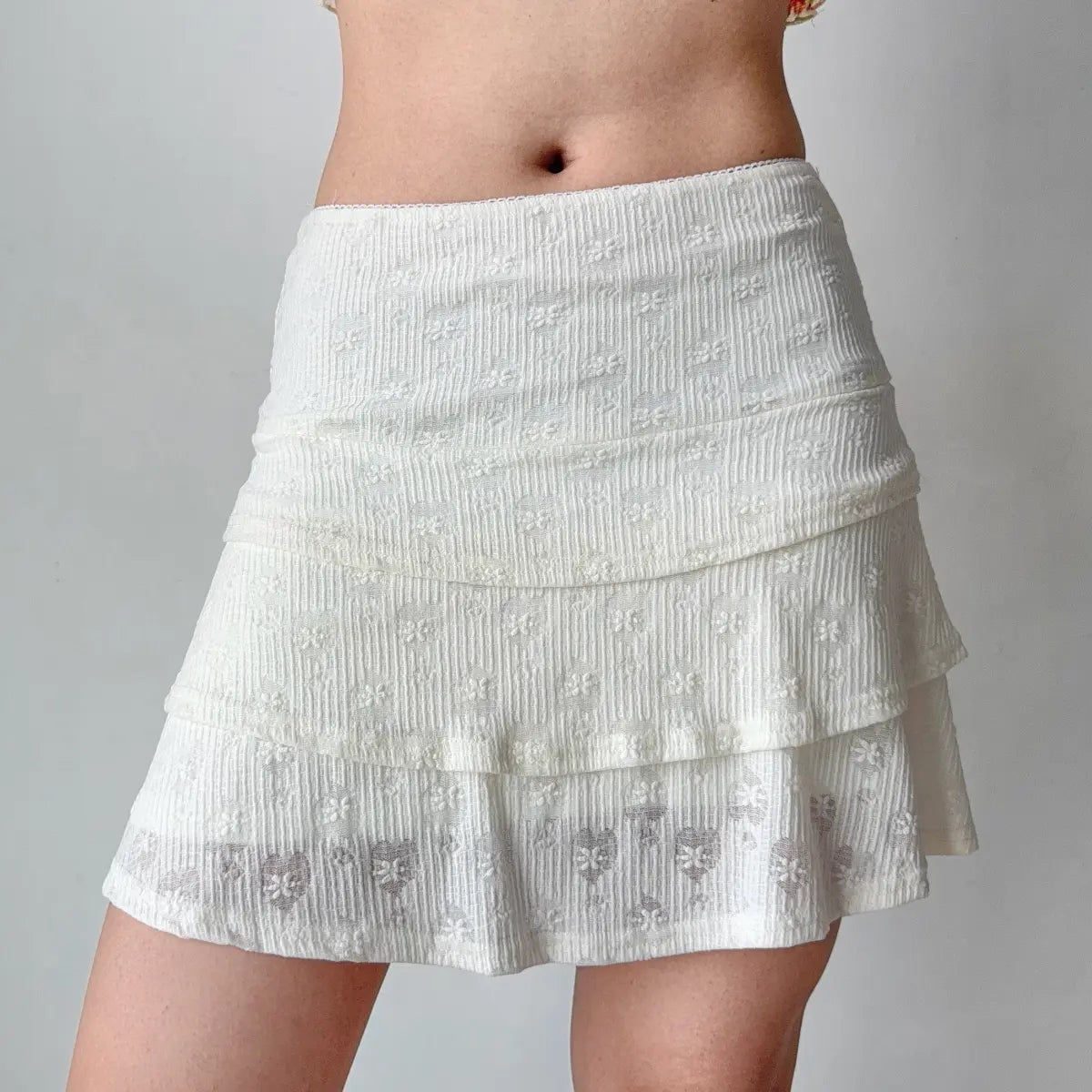 Side view of a white floral lace tiered mini skirt, highlighting the layered construction and textured fabric.