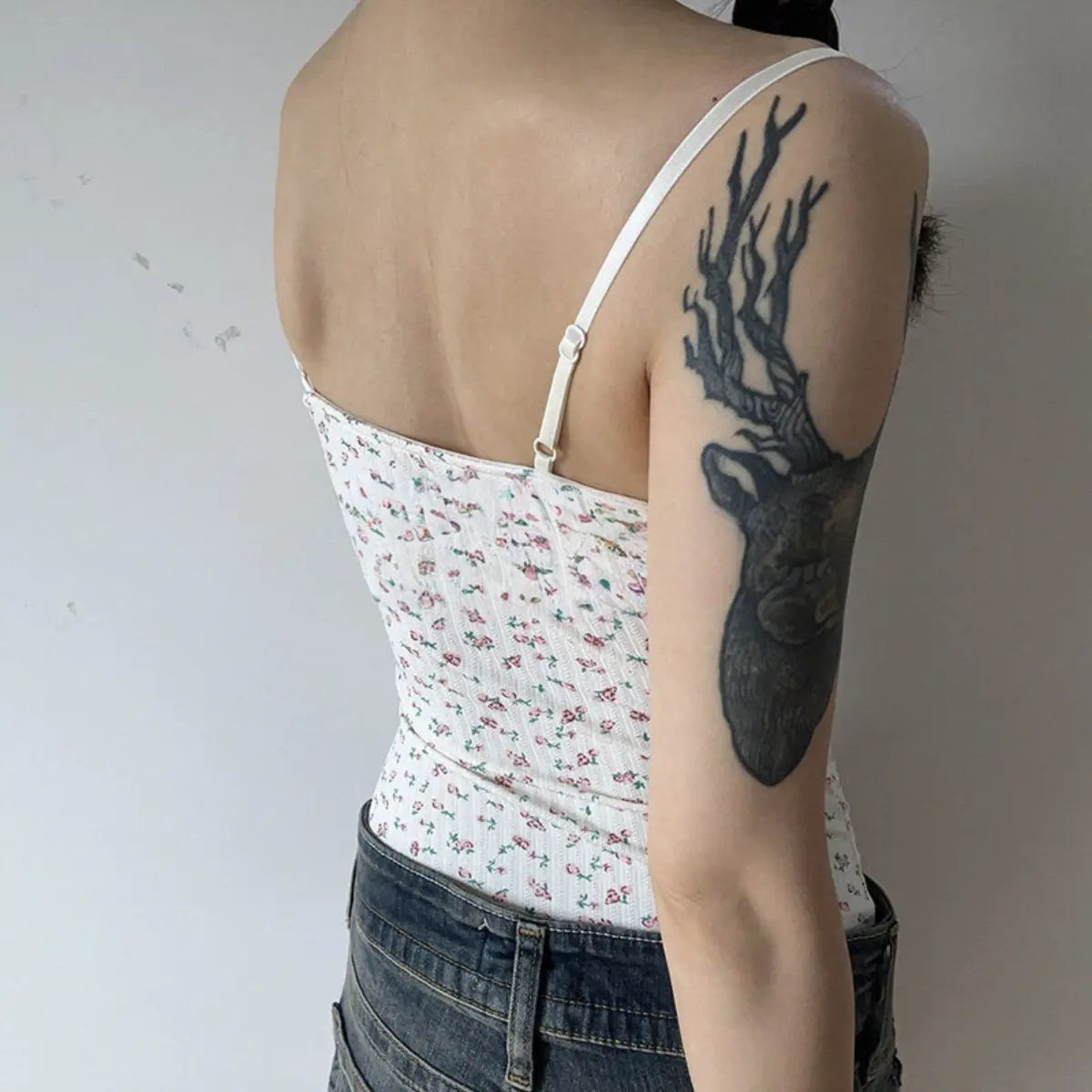 Back view of a woman wearing a white floral lace-trimmed cami top, showing the adjustable strap and tattoo on her arm.