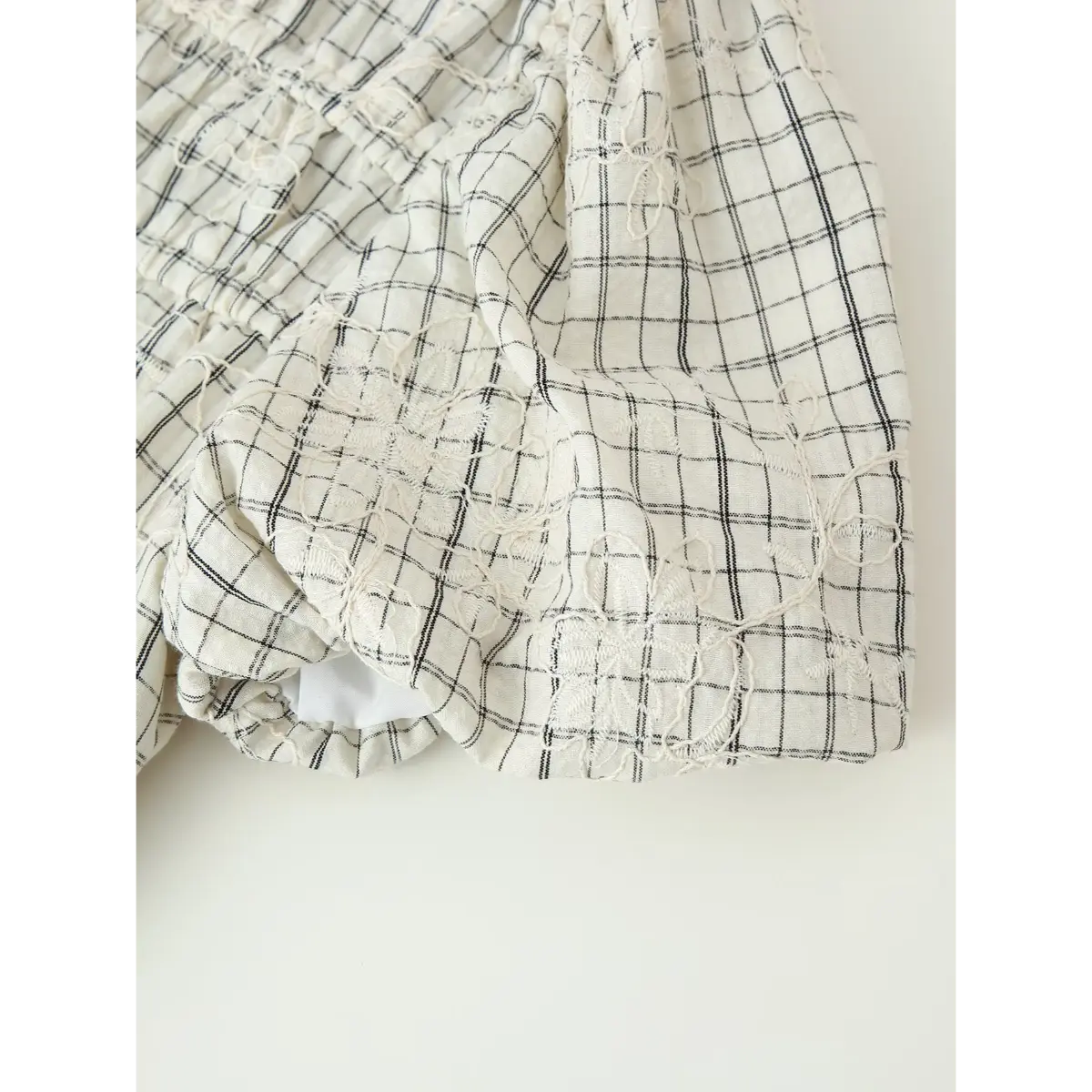 Close-up of the puff sleeve on the white grid embroidered top, showing the gathered cuff, floral embroidery, and black grid pattern