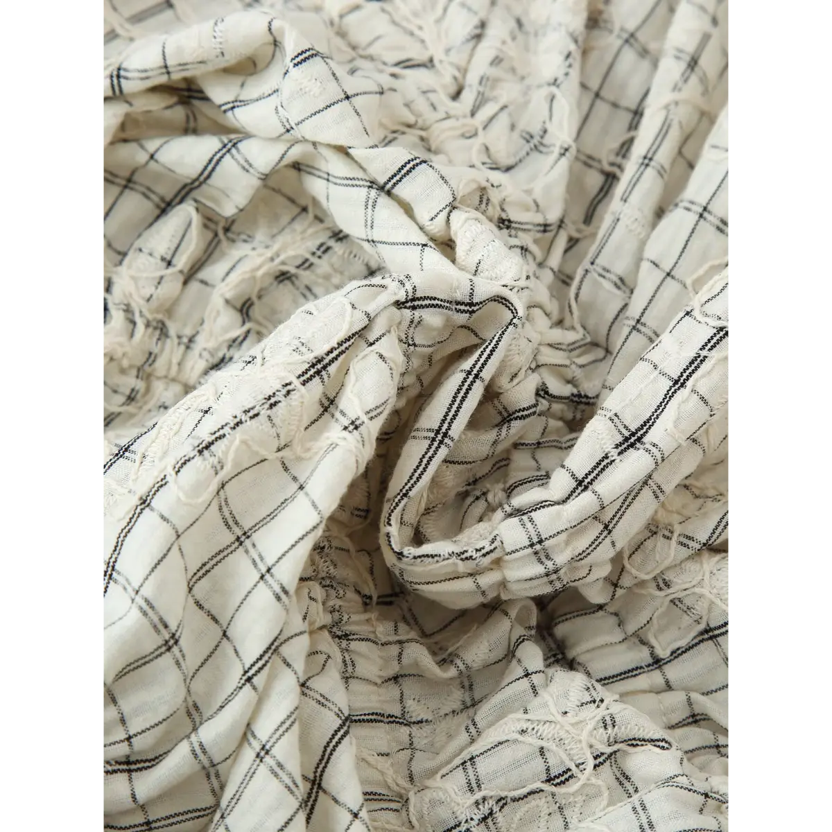 Close-up of the fabric texture on the white grid embroidered top, showing the crinkled weave, grid pattern, and raised floral embroidery