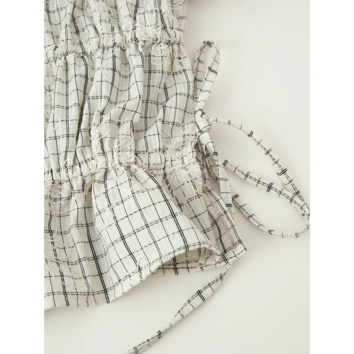 Close-up of the side drawstring on the white grid embroidered top, showing the matching fabric tie and tiered construction