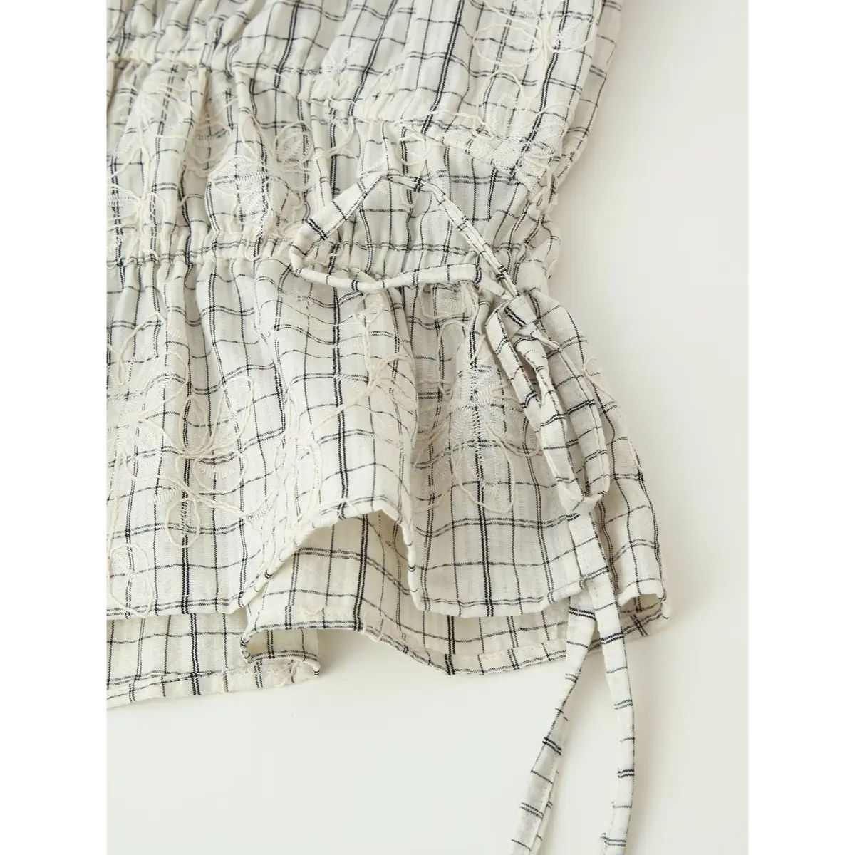 Close-up of the side tie and ruffled tier on the white grid embroidered top, showing the gathered drawstring