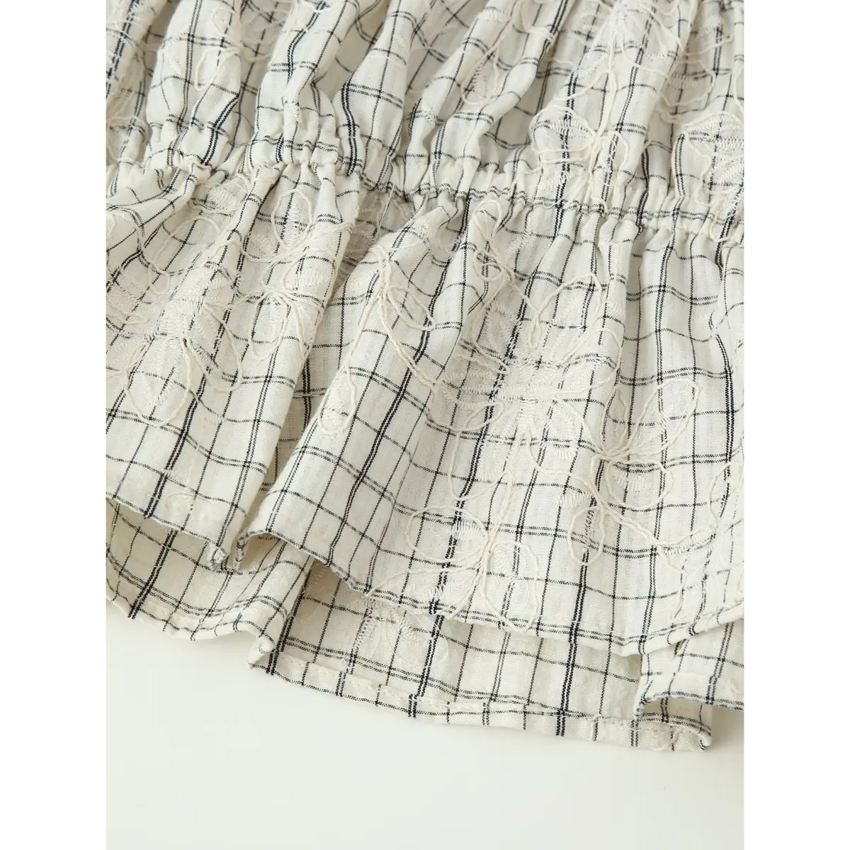 Close-up of the tiered hem on the white grid embroidered top, showing the ruffled layers and floral embroidery details