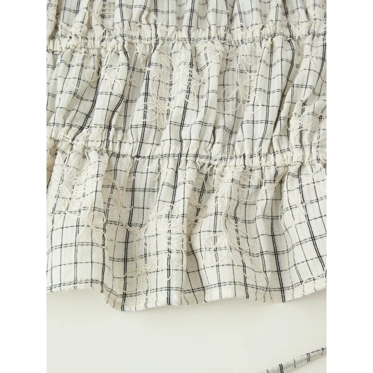 Close-up of the tiered skirt on the white grid embroidered top, showing multiple gathered layers and repeating floral embroidery