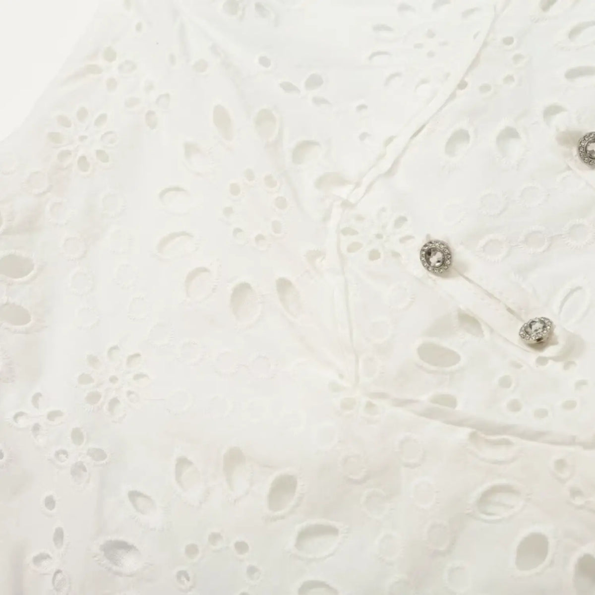 Close-up of eyelet embroidery and rhinestone buttons on white dress