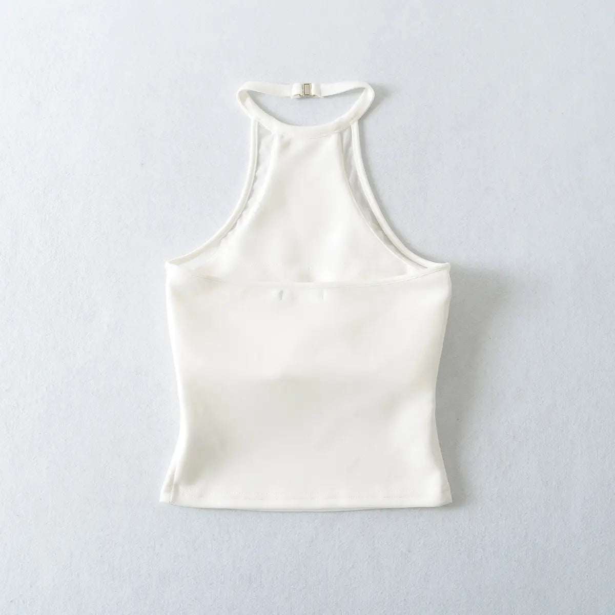 Back view of a white halter-neck top, showing the smooth fabric, adjustable clasp, and finished seams.
