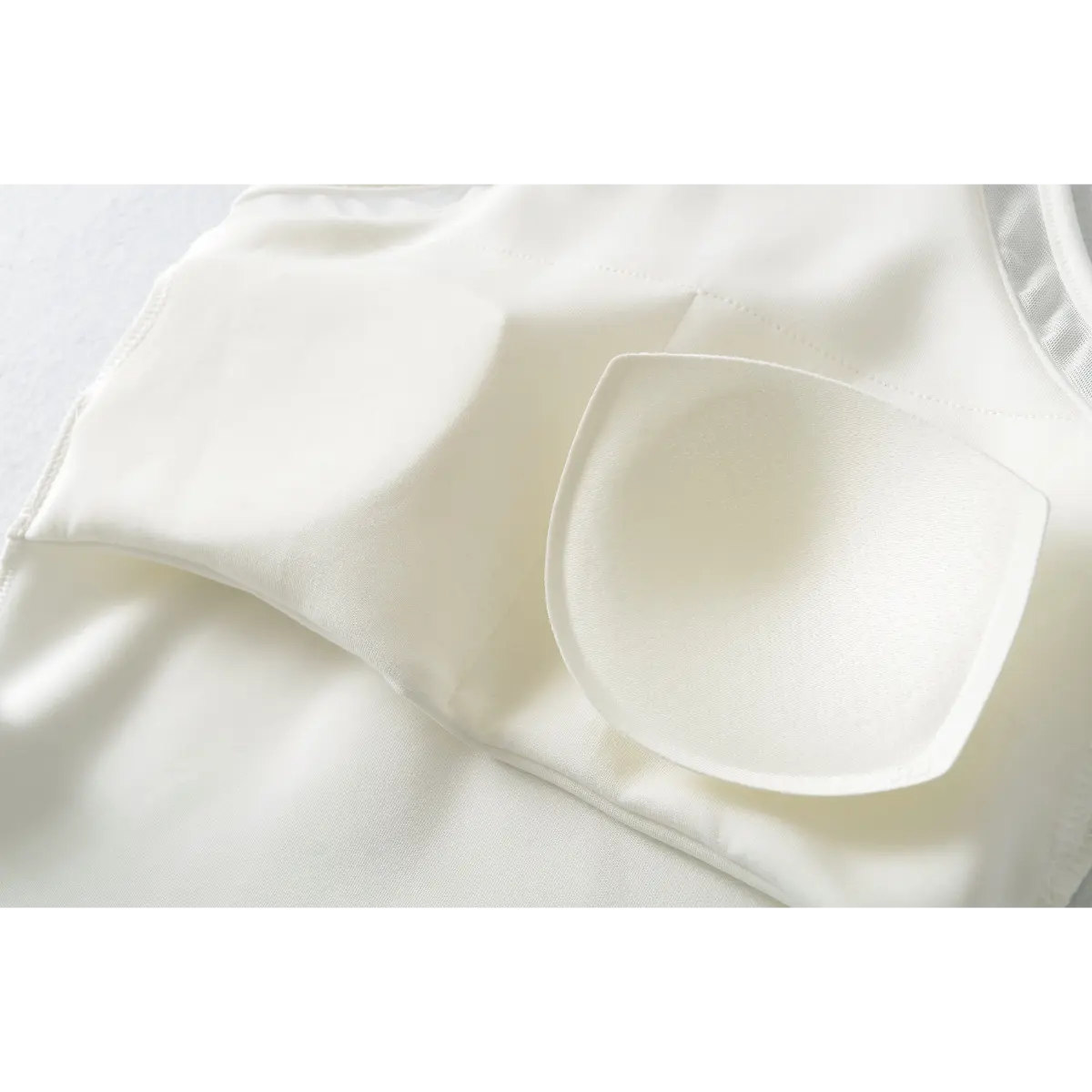 Close-up of the removable bra pad inside a white halter-neck top, showing the soft, molded design and inner lining.