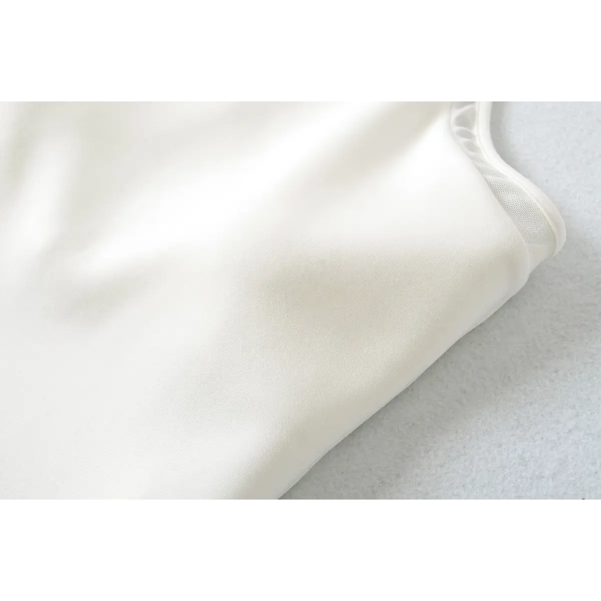 Close-up of the fabric texture on a white halter-neck top, showing the smooth, stretchy material and mesh panel.
