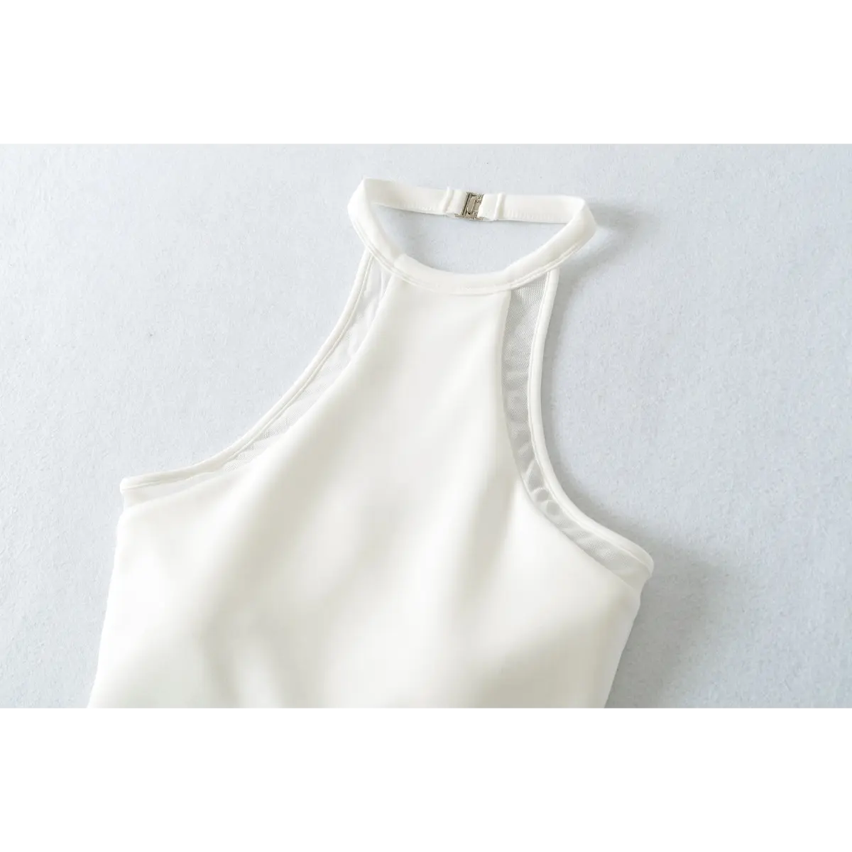 Close-up of the front of a white halter-neck top, highlighting the mesh panels and metal clasp closure.
