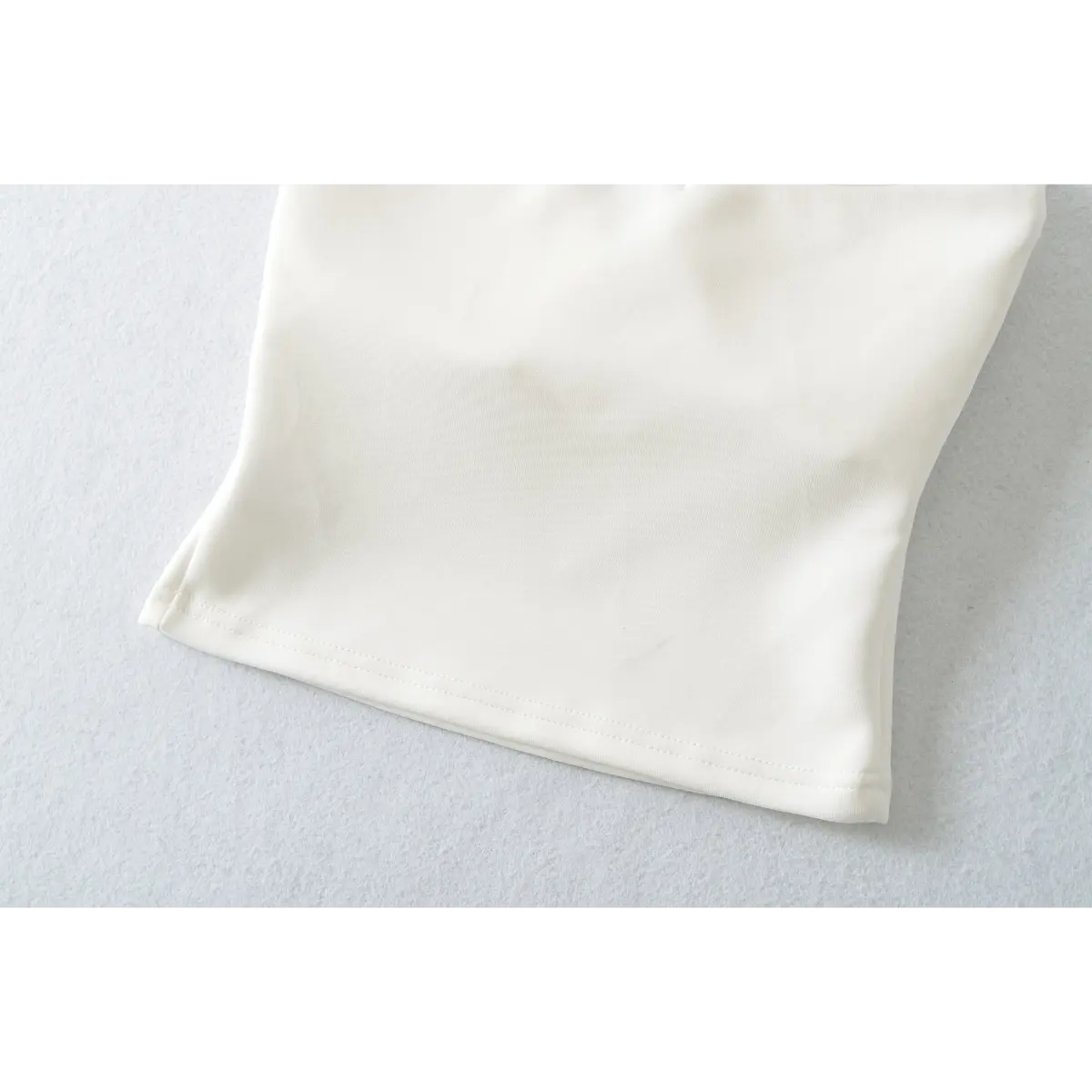 Close-up of the hem on a white halter-neck top, showing the clean stitching and stretchy fabric.